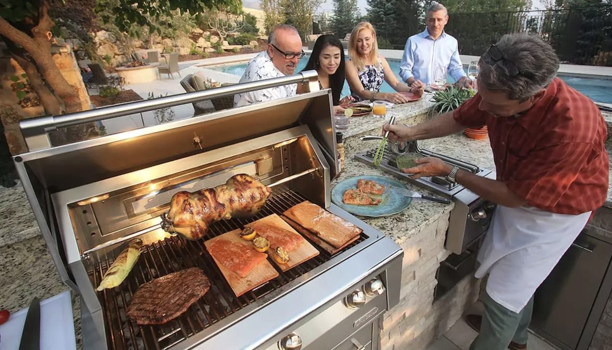 people watching man grilling in outdoor kitchen