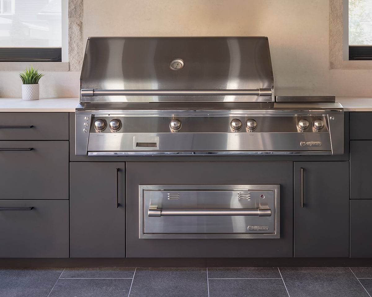 Alfresco stainless warming drawer installed beneath built-in grill in charcoal-grey outdoor kitchen cabinetry