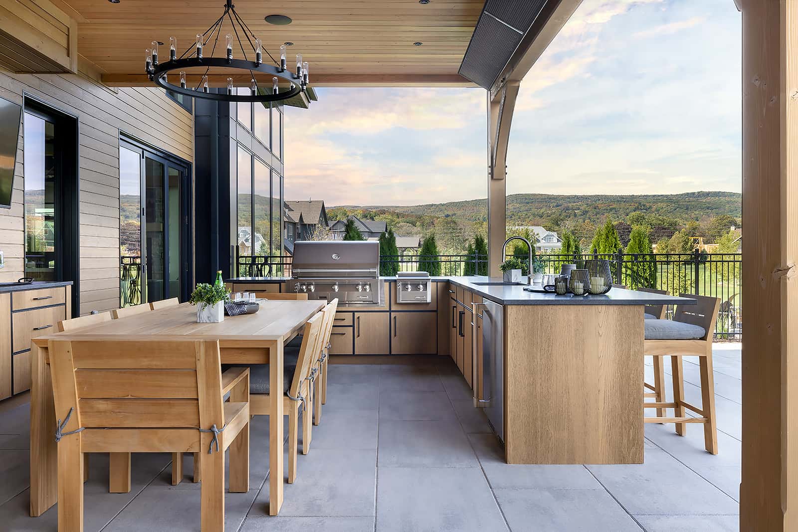 Modern L-shaped outdoor kitchen with NatureKast cabinetry, built-in grill, dining table, and scenic view