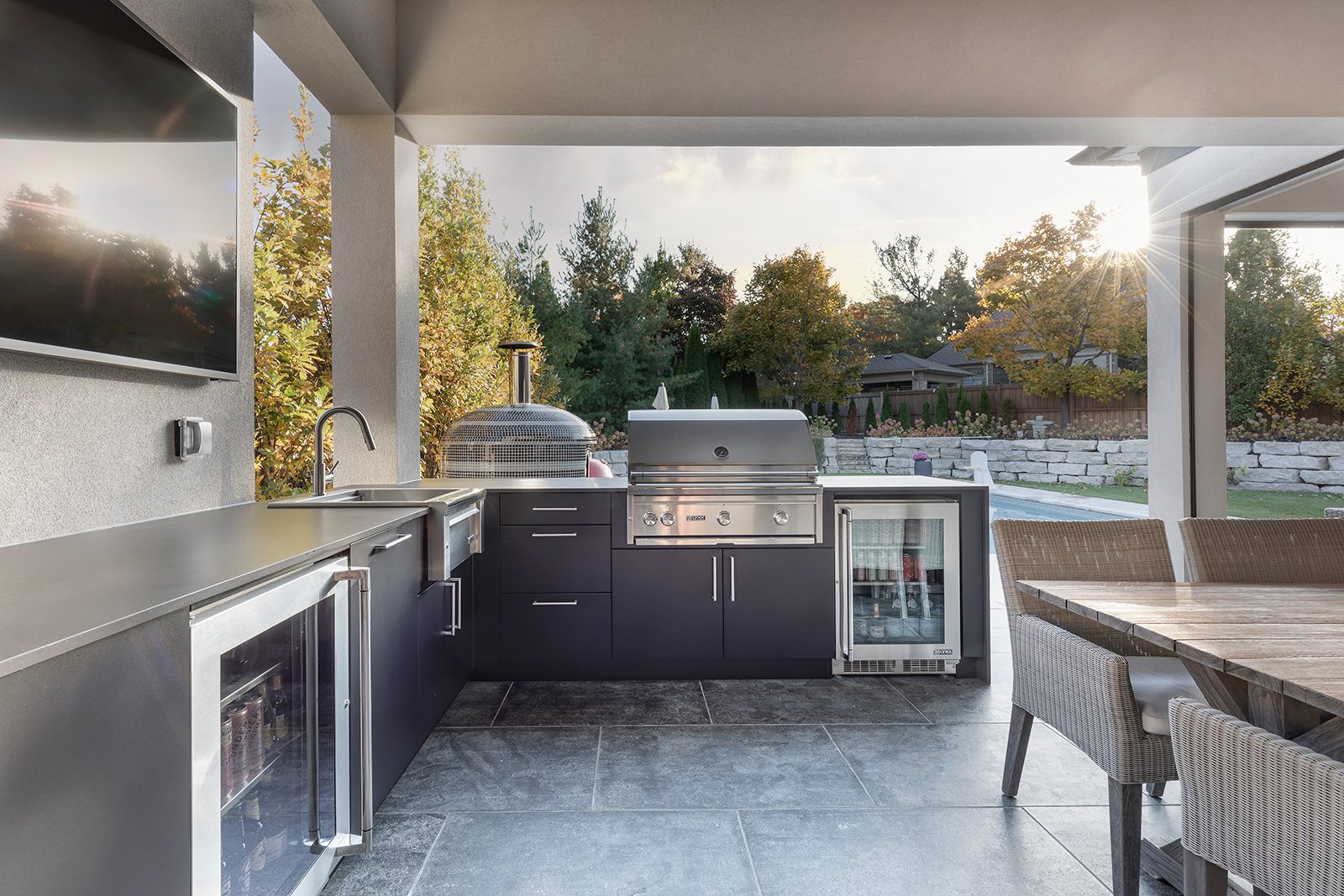 l-shaped outdoor kitchen with grill, fridge, dining table and pool in the background