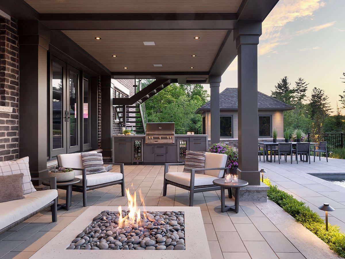 Backyard at dusk featuring a stone fire pit lounge, covered grill station, and separate dining area beside a pool