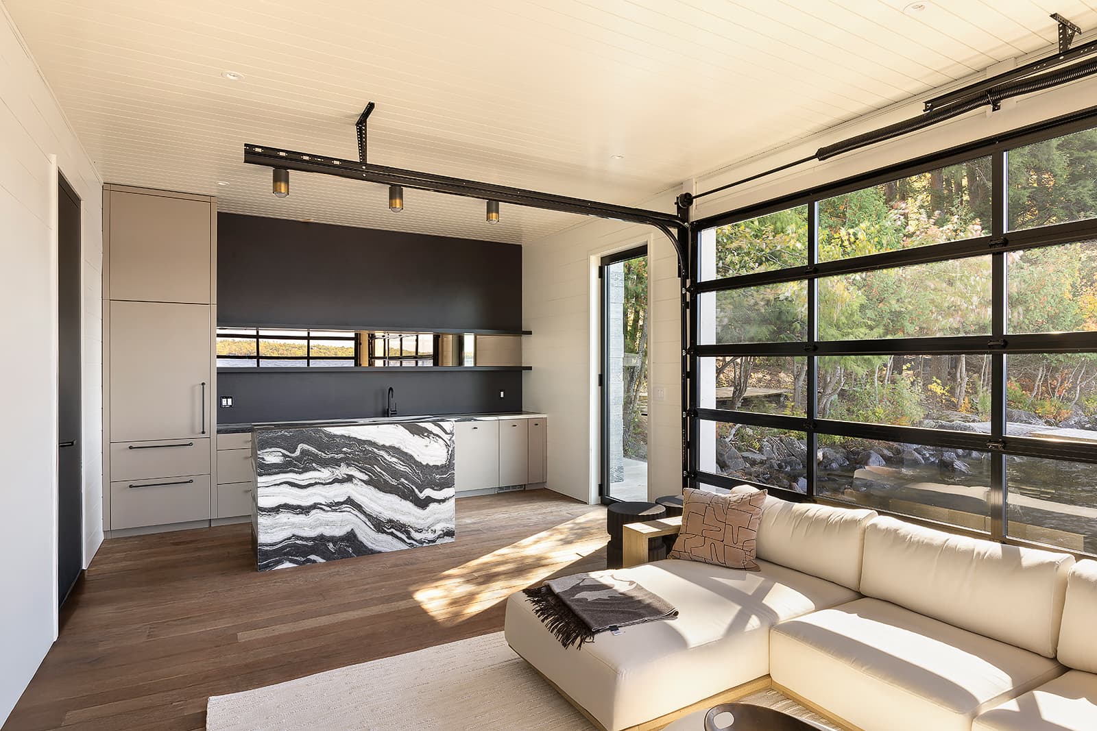 Luxury Muskoka boathouse kitchen with Alumina cabinetry, dramatic marble island, and glass garage door overlooking the water