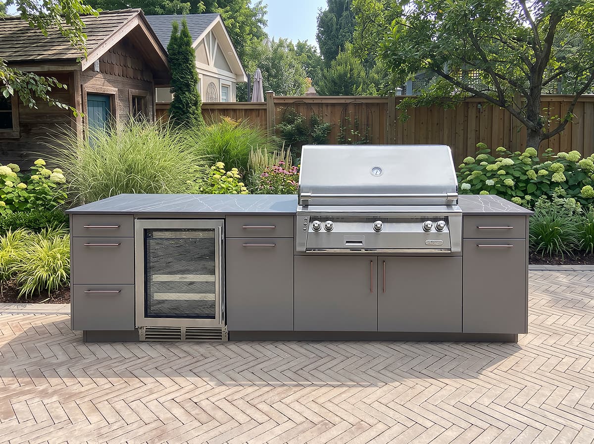 Grey Alumina Architectural Surfaces outdoor kitchen cabinetry with a built-in stainless steel grill and beverage fridge on a herringbone brick patio.