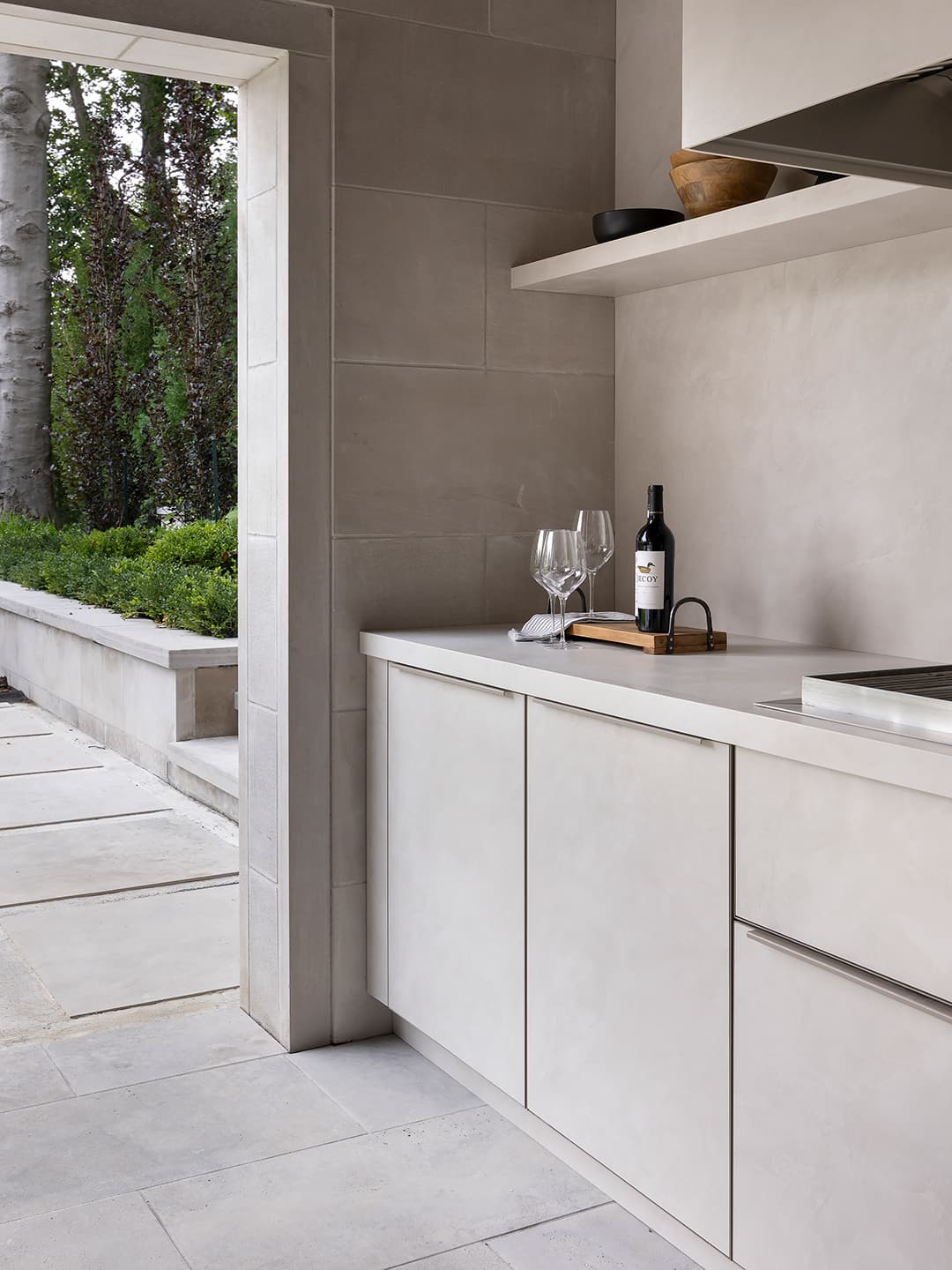 Modern covered terrace outdoor kitchen featuring flush limestone cabinetry wine bottle and glasses