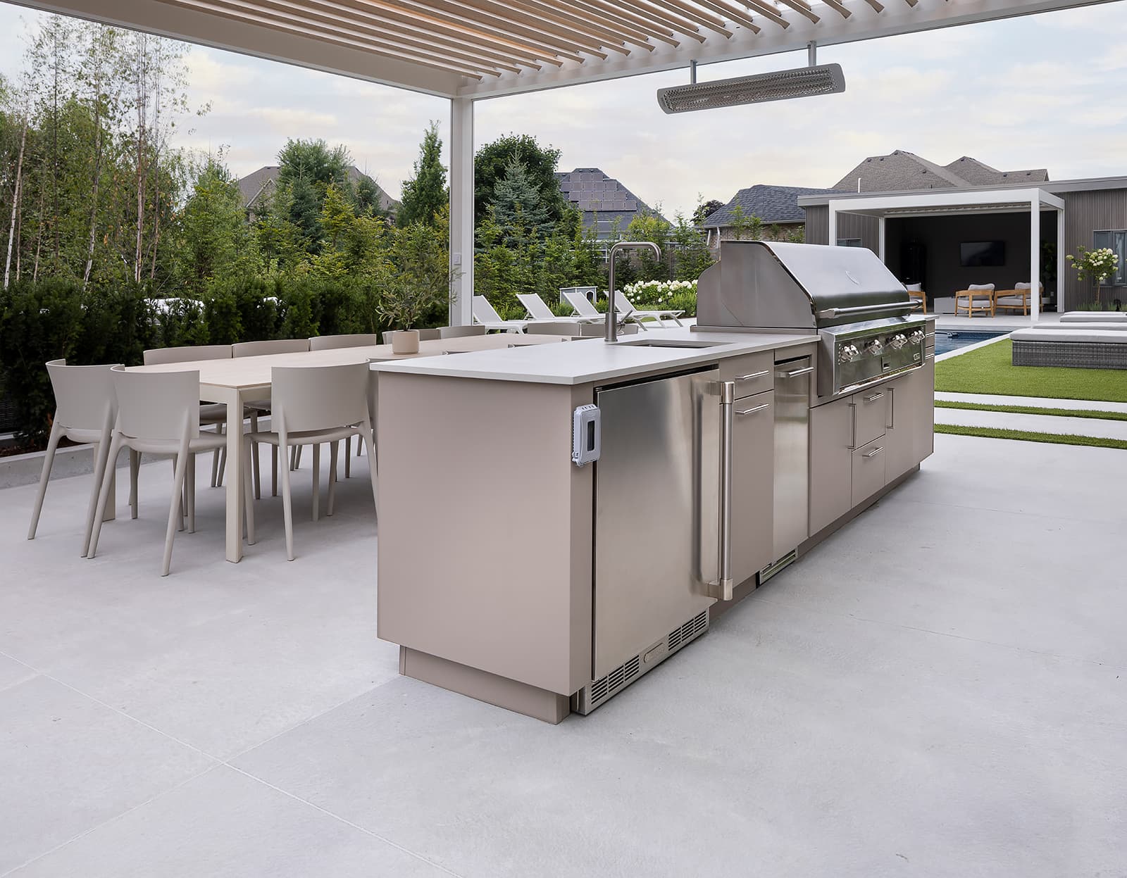 outdoor kitchen in backyard under a pergola beside a pool