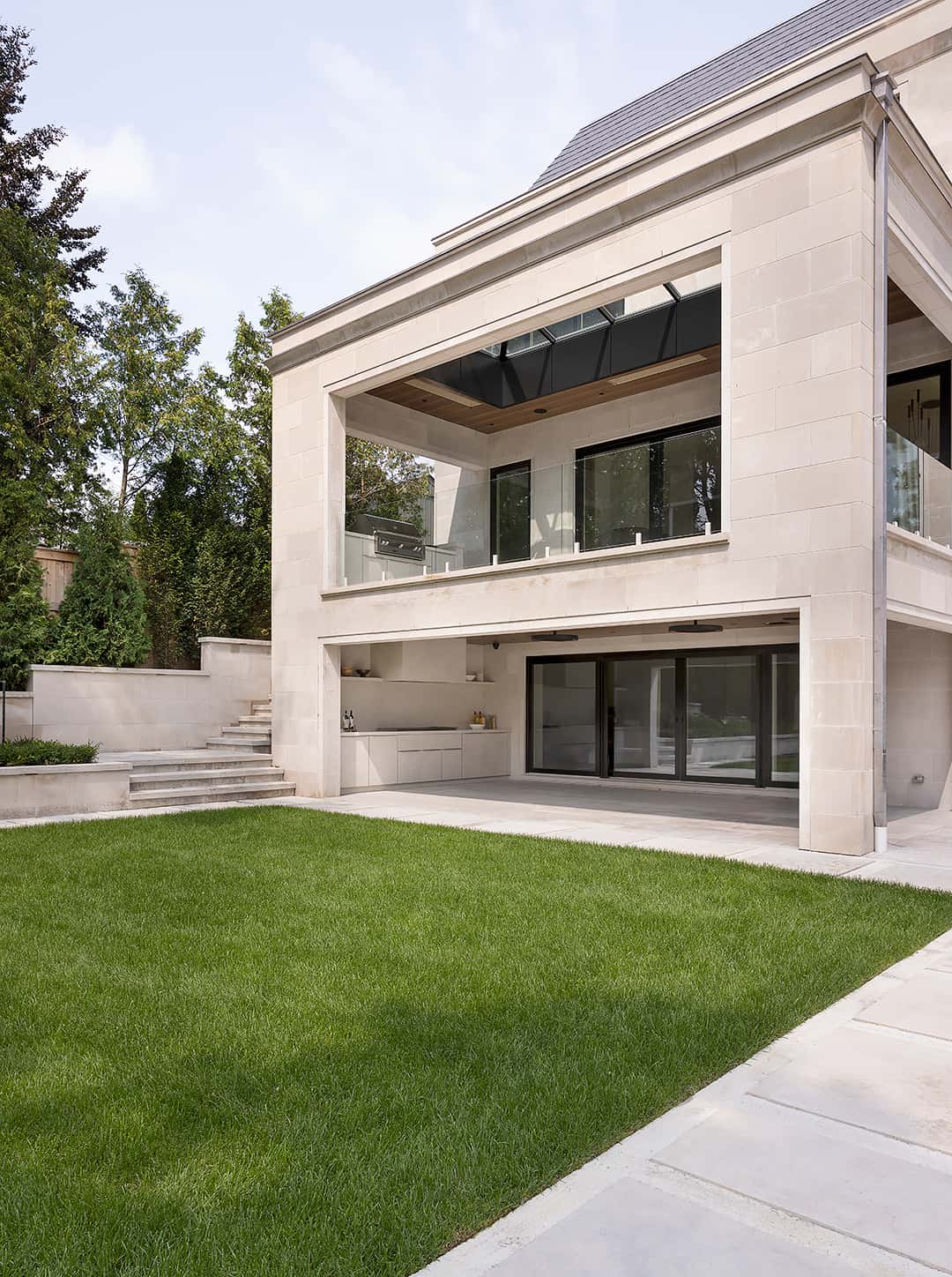 Modern two tier outdoor kitchen and covered stone patio on a manicured lawn