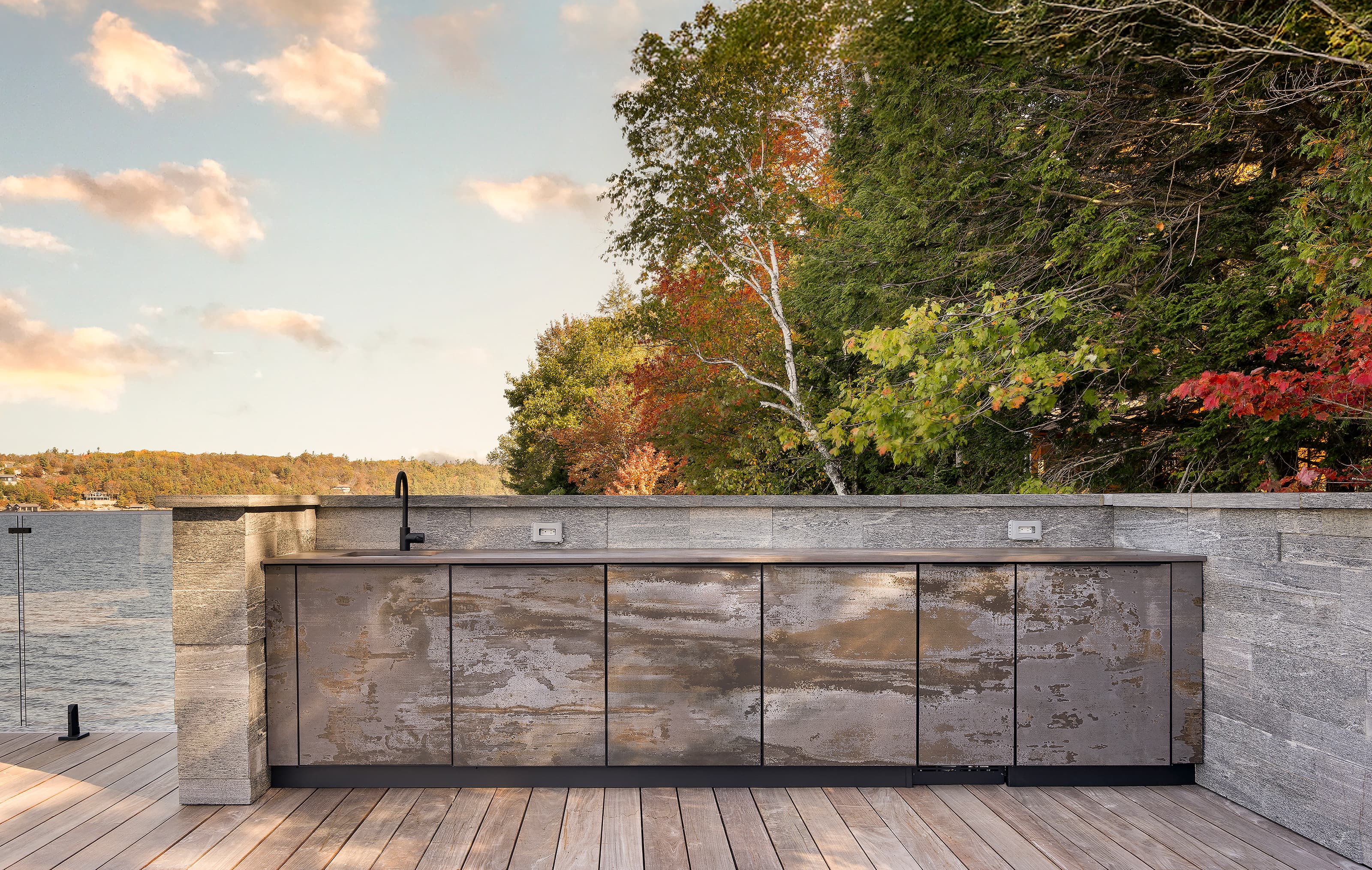 Galley-style outdoor kitchen cabinetry on the upper deck of a Muskoka boathouse, featuring weather-resistant finishes, integrated sink, and lakefront views.