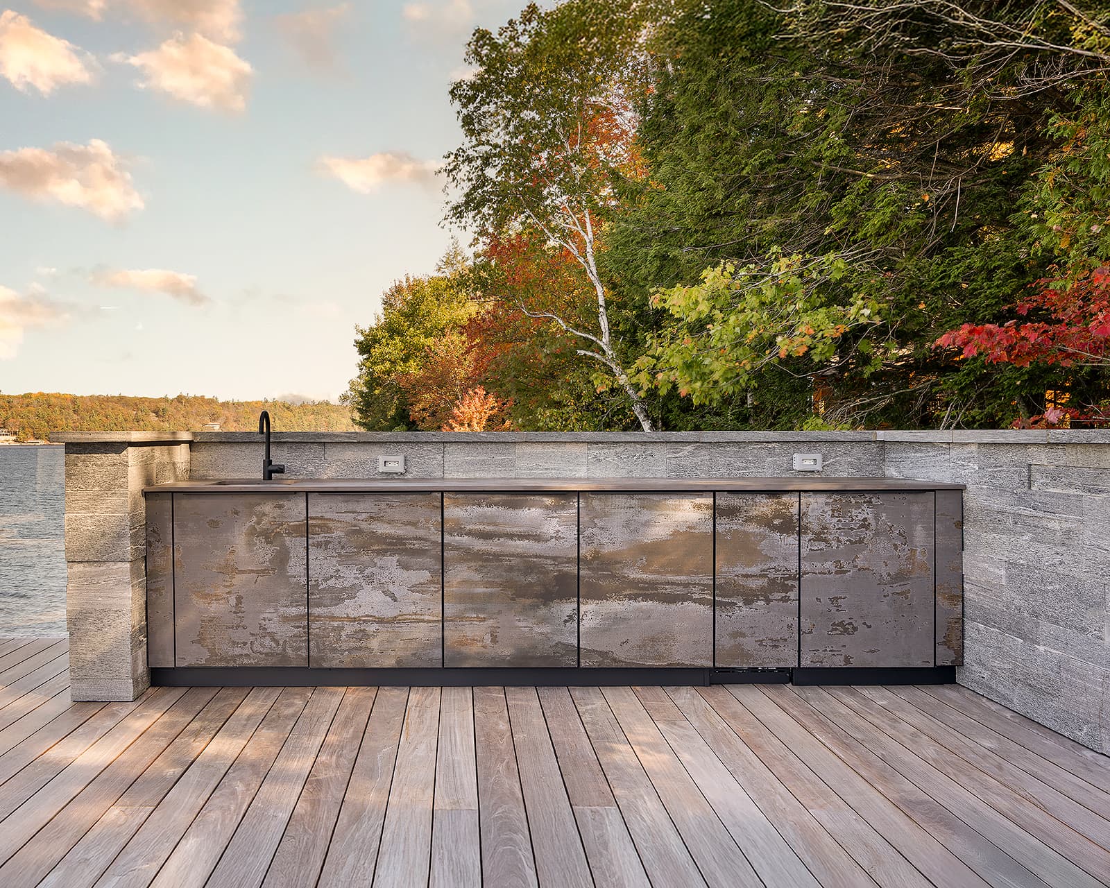 Galley-style outdoor kitchen cabinetry on the upper deck of a Muskoka boathouse, featuring weather-resistant finishes, integrated sink, and lakefront views.