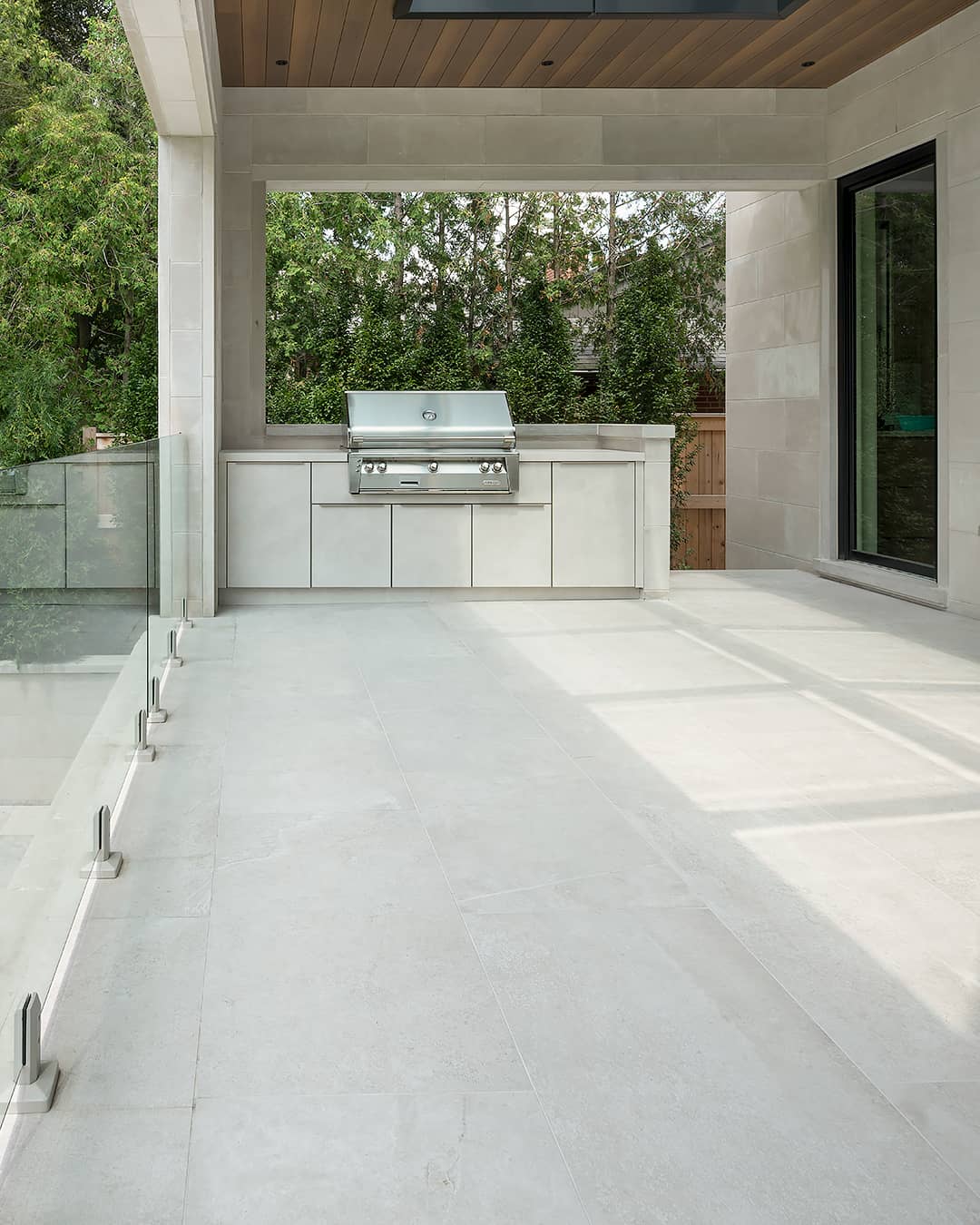 Covered stone terrace featuring a built in stainless steel barbecue and modern glass railing