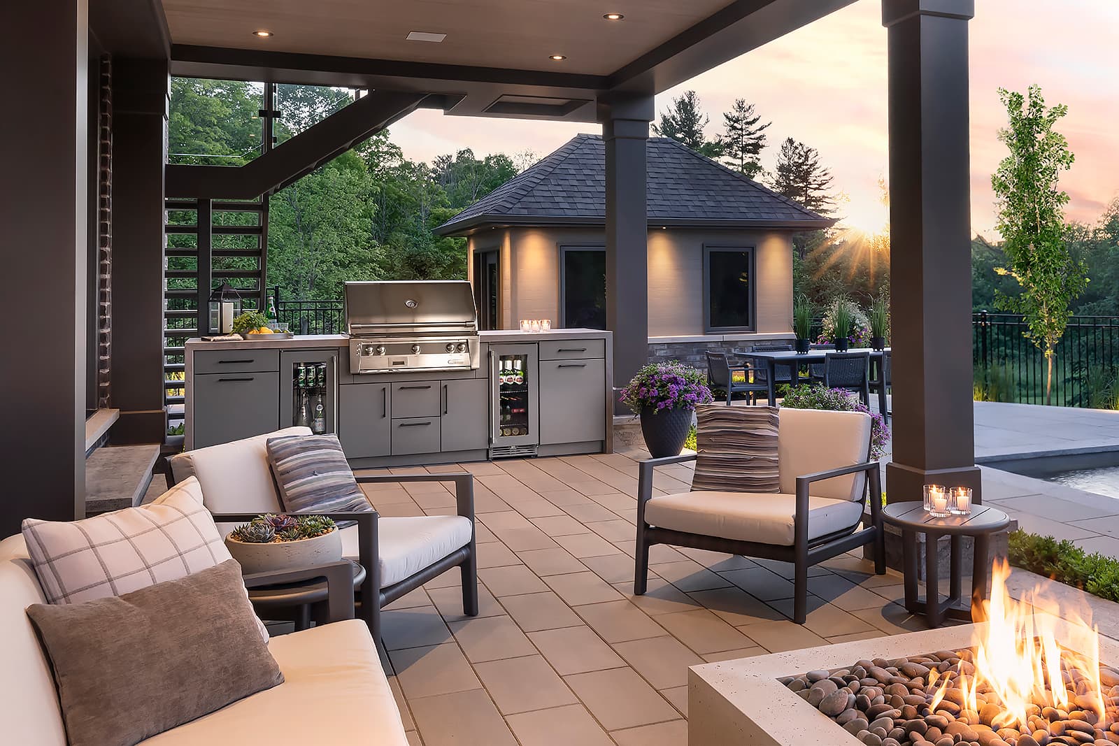luxurious outdoor kitchen in a backyard at sunset with a pool and fire pit