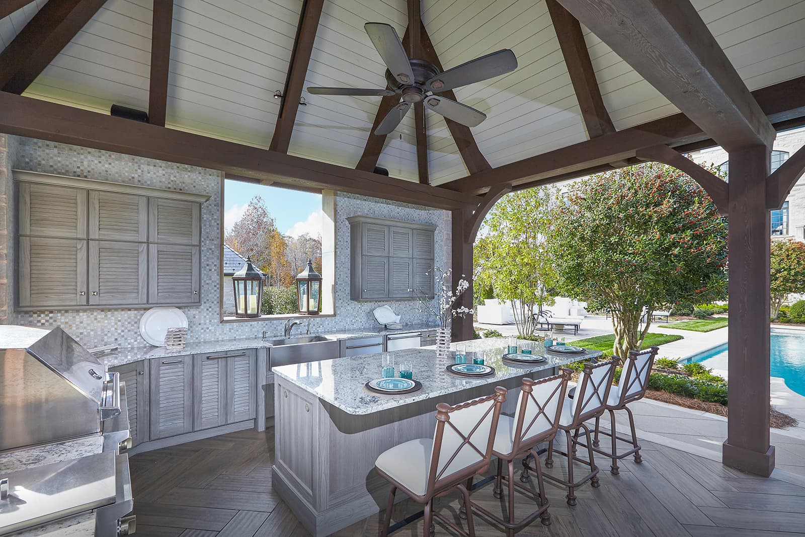 Covered outdoor kitchen near pool with NatureKast cabinetry and island for seating